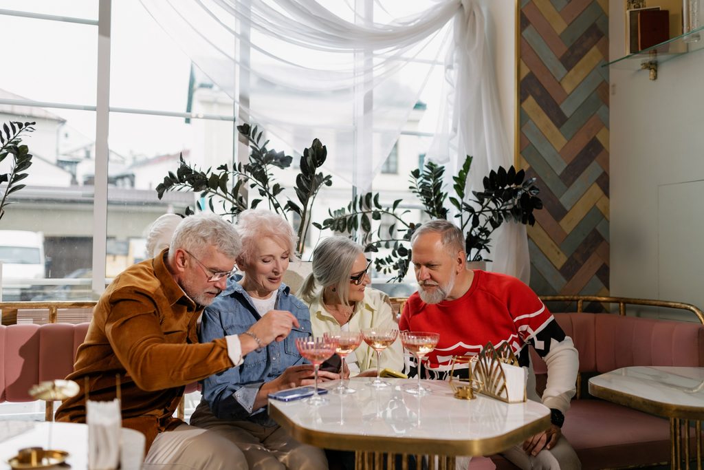 imagen de 4 adultos mayores, 2 hmbre y 2 mujeres, conversando y tomando una copa cada uno