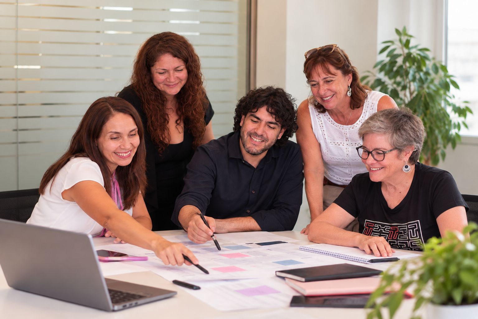Equipo de 5 personas sentadas alrededor de una mesa trabajando 